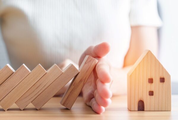Hand stopping wooden dominoes falling on wooden house