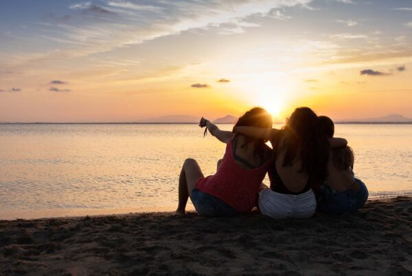 Friends sitting on beach looking at sunset
